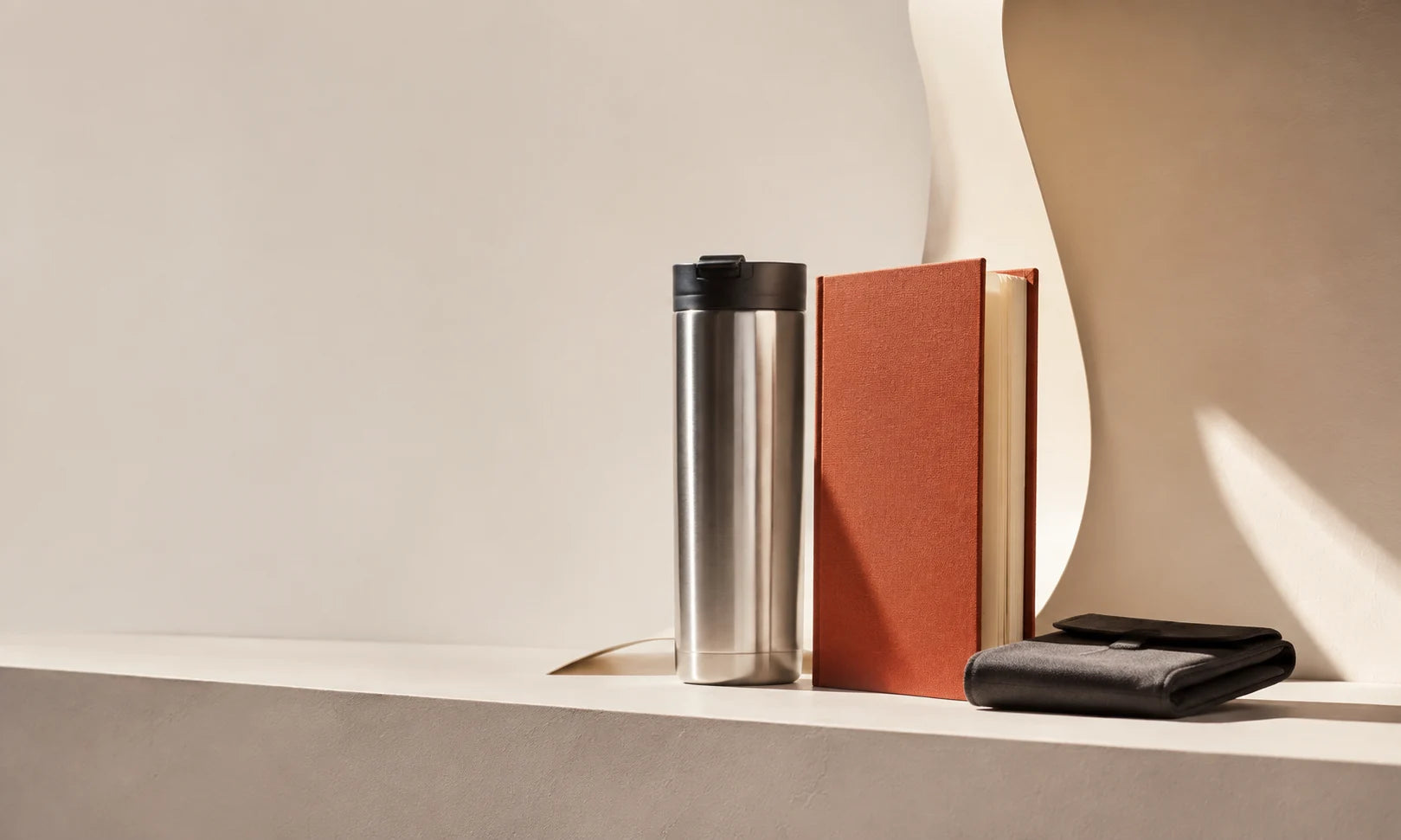 Illustrative client gift concept with a brushed metal vessel, terracotta notebook and charcoal pouch