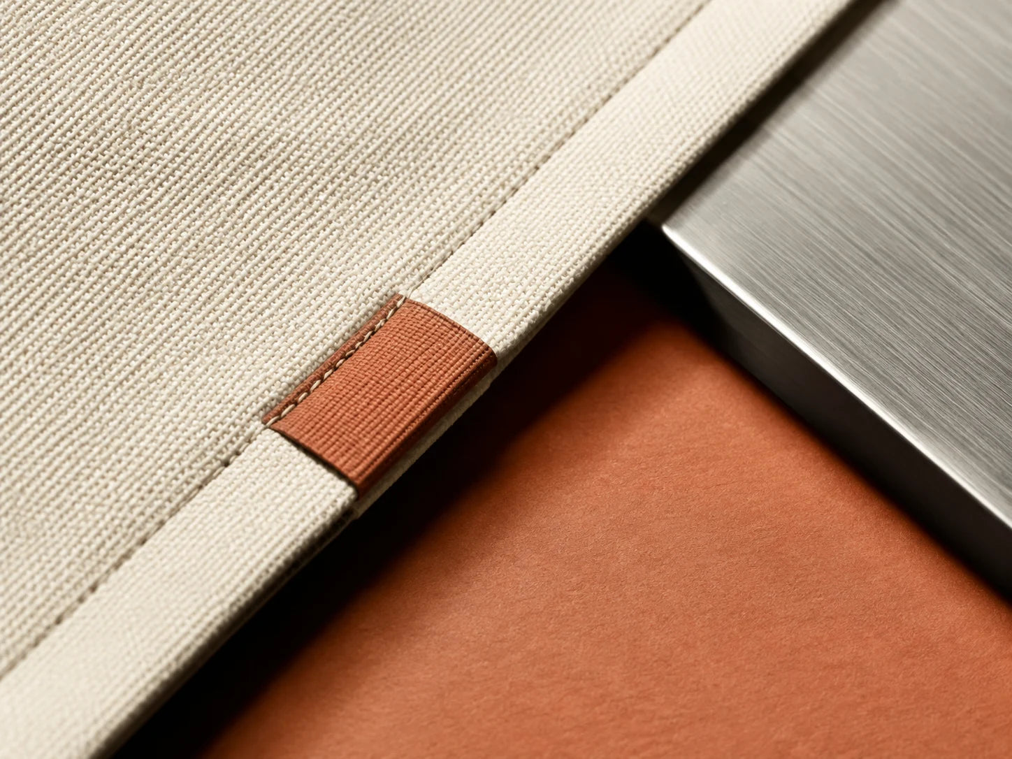 Illustrative close-up of canvas stitching, a terracotta cloth label and brushed metal