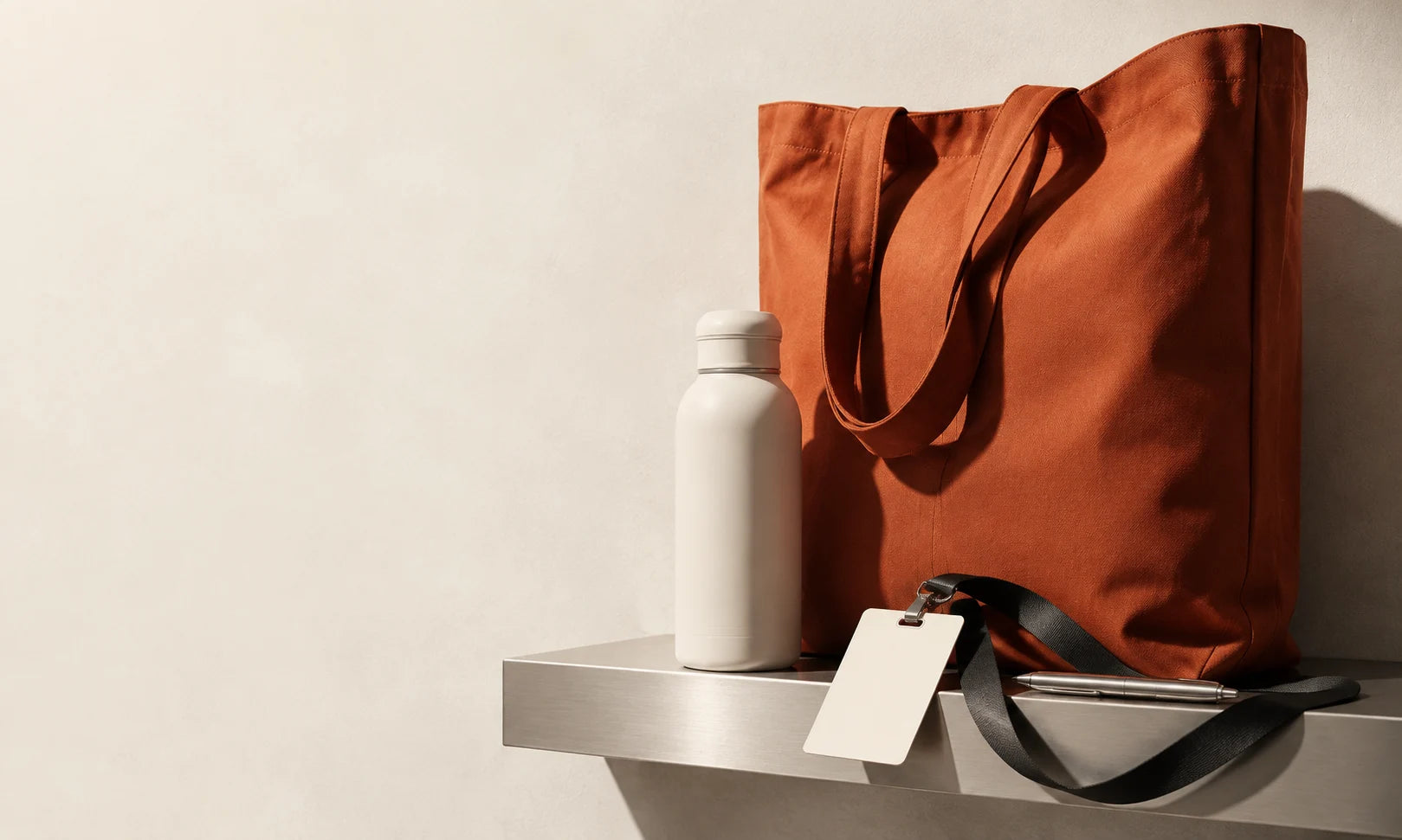 Illustrative event concept with a terracotta tote, ivory bottle and blank badge on a charcoal lanyard
